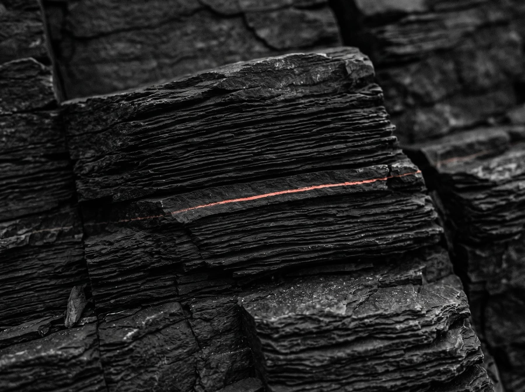 Close-up of thin dark slate strata stacked like sheets of paper, one seam marked in orange